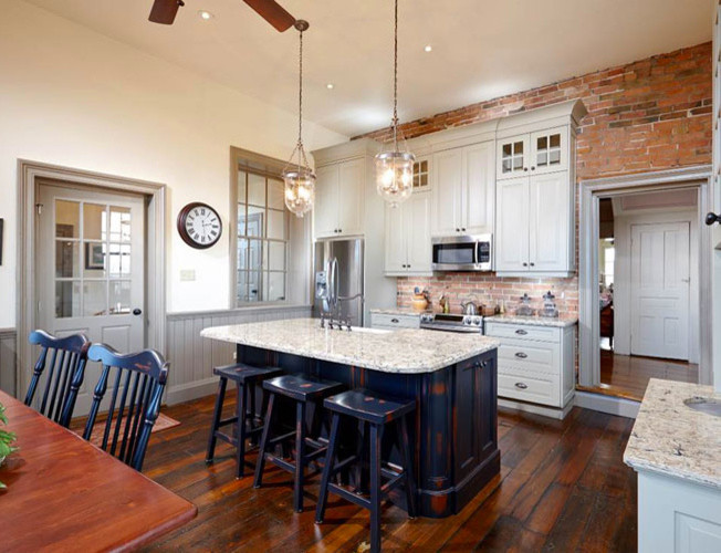 Lantlig inredning av ett mellanstort kök, med en rustik diskho, luckor med upphöjd panel, granitbänkskiva, rostfria vitvaror, mellanmörkt trägolv, en köksö, vita skåp, rött stänkskydd och stänkskydd i stenkakel