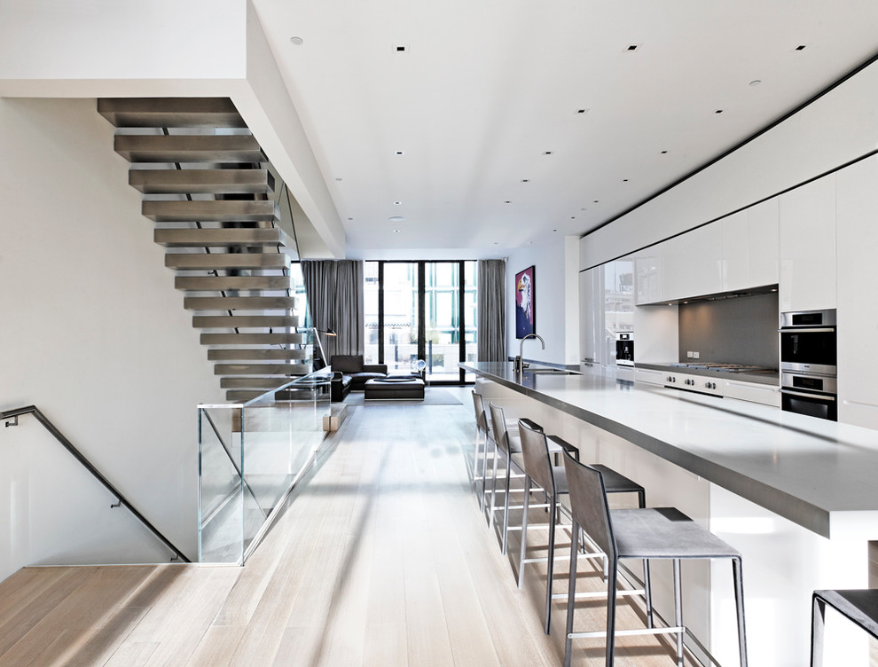 This is an example of a modern galley kitchen in New York with flat-panel cabinets, white cabinets, grey splashback and stainless steel appliances.