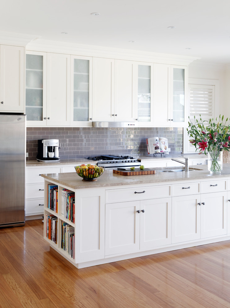 Medium sized classic galley open plan kitchen in Sydney with a submerged sink, recessed-panel cabinets, white cabinets, marble worktops, grey splashback, glass tiled splashback, stainless steel appliances, medium hardwood flooring and an island.