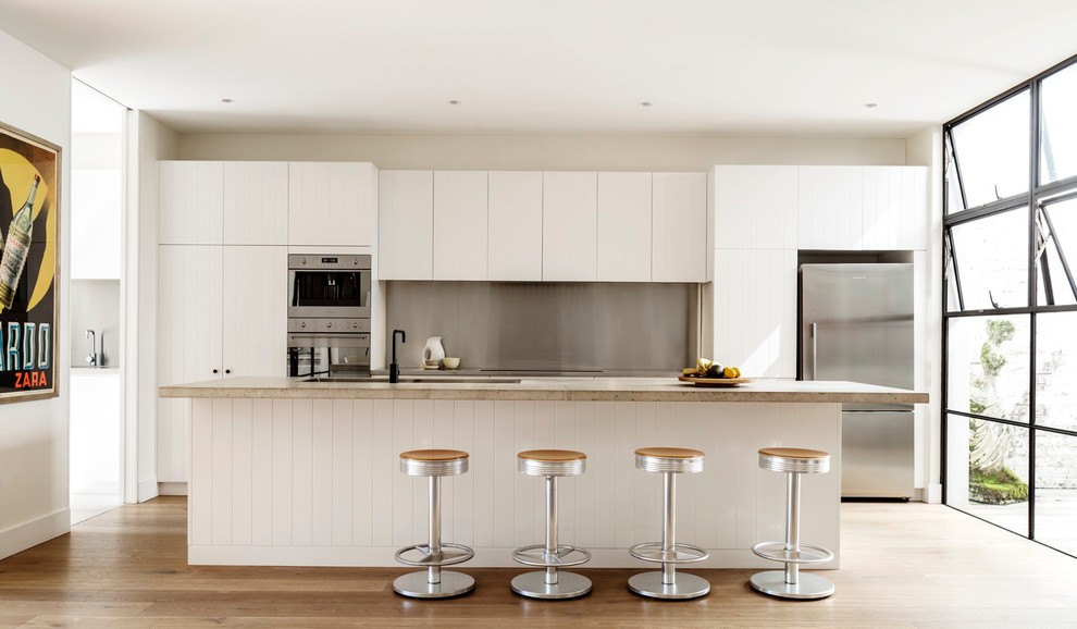 Zweizeilige Moderne Küche mit Unterbauwaschbecken, flächenbündigen Schrankfronten, weißen Schränken, Küchenrückwand in Metallic, Küchengeräten aus Edelstahl, hellem Holzboden, Kücheninsel und beigem Boden in Sydney