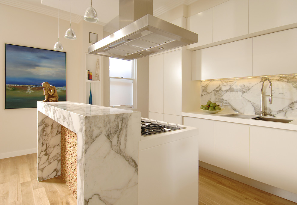 Huge minimalist u-shaped light wood floor, beige floor and tray ceiling open concept kitchen photo in Sydney with recessed-panel cabinets, an island, an undermount sink, white cabinets, solid surface countertops, white backsplash, marble backsplash, stainless steel appliances and white countertops