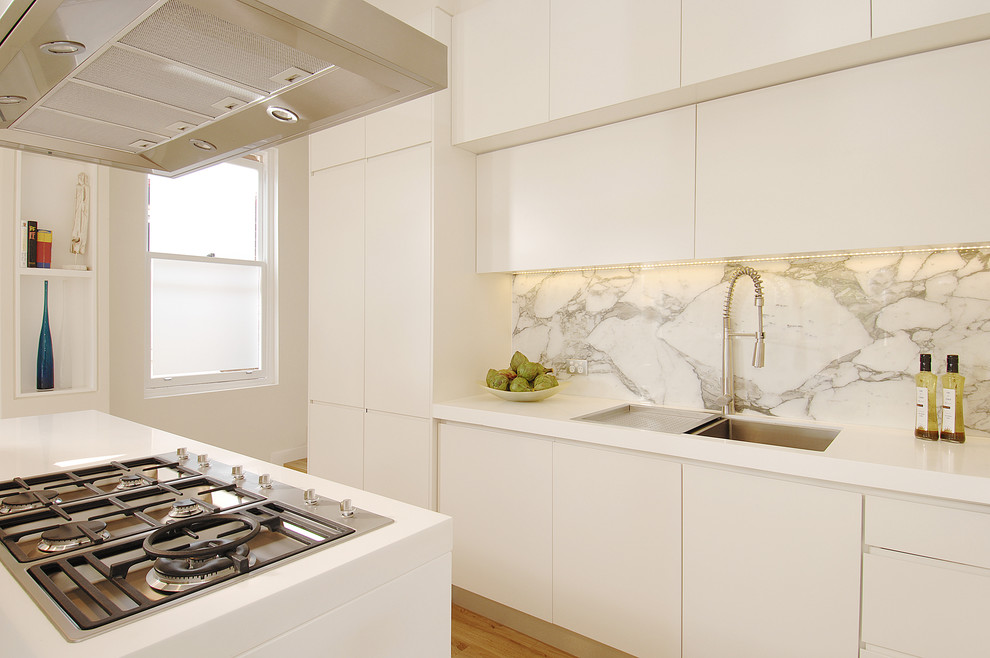 Photo of an expansive modern grey and white u-shaped open plan kitchen in Sydney with recessed-panel cabinets, an island, a submerged sink, white cabinets, composite countertops, white splashback, marble splashback, stainless steel appliances, light hardwood flooring, beige floors, white worktops and a drop ceiling.