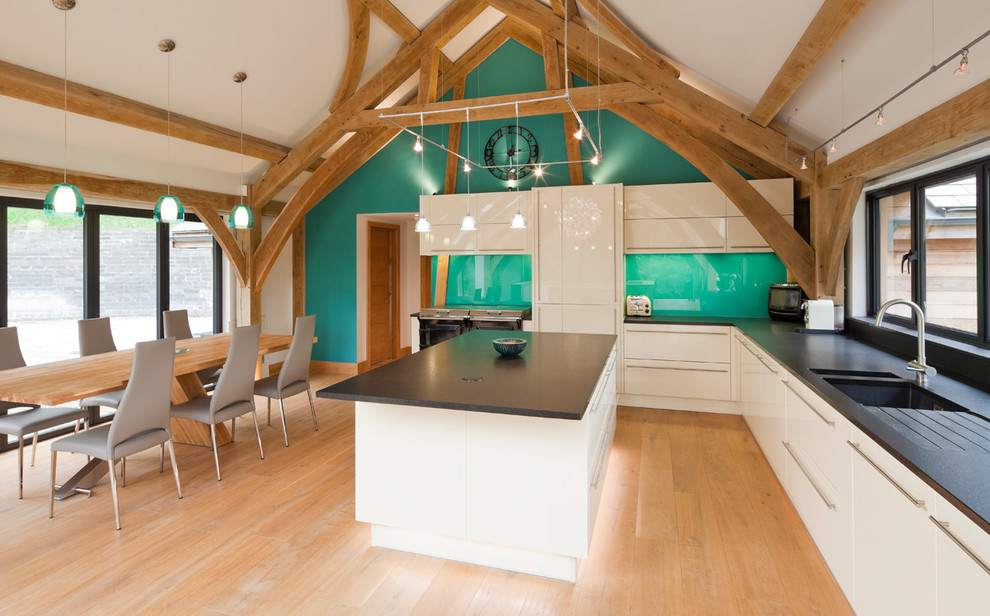 Moderne Wohnküche in L-Form mit Unterbauwaschbecken, flächenbündigen Schrankfronten, weißen Schränken, Küchengeräten aus Edelstahl, braunem Holzboden, Kücheninsel und braunem Boden in Sussex