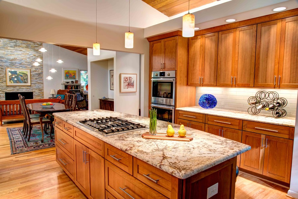 Exemple d'une cuisine parallèle tendance avec un plan de travail en granite, une crédence blanche, une crédence en carreau de verre, un électroménager en acier inoxydable, un sol en bois brun et îlot.