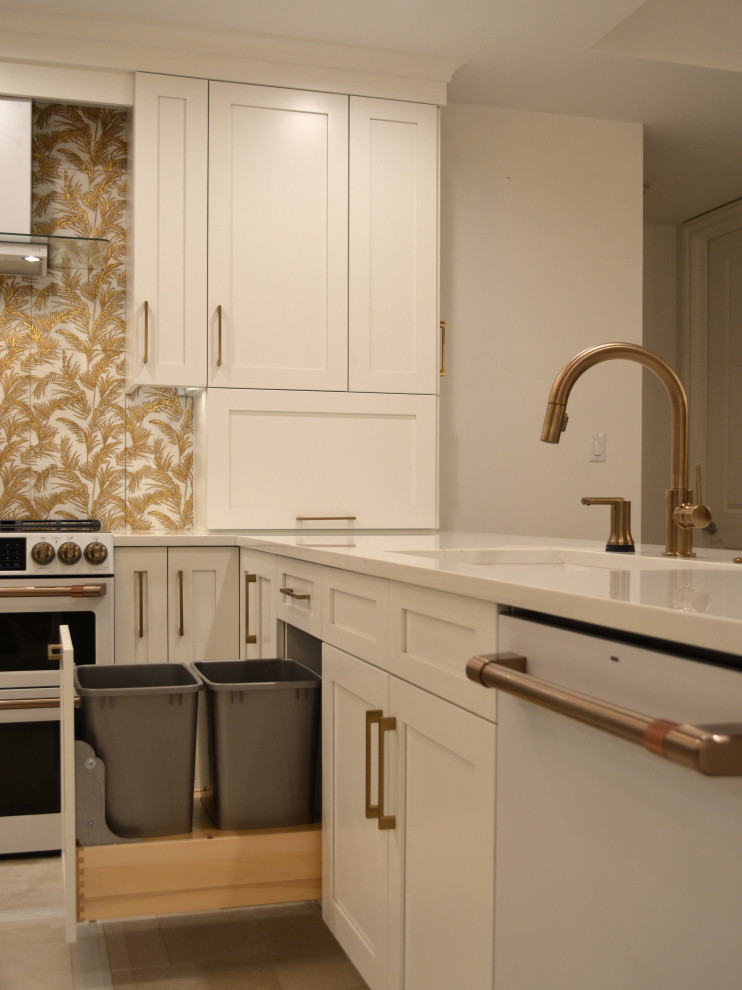 Klassisk inredning av ett stort vit vitt kök, med en undermonterad diskho, skåp i shakerstil, vita skåp, bänkskiva i kvarts, stänkskydd med metallisk yta, stänkskydd i porslinskakel, vita vitvaror, marmorgolv, en köksö och beiget golv