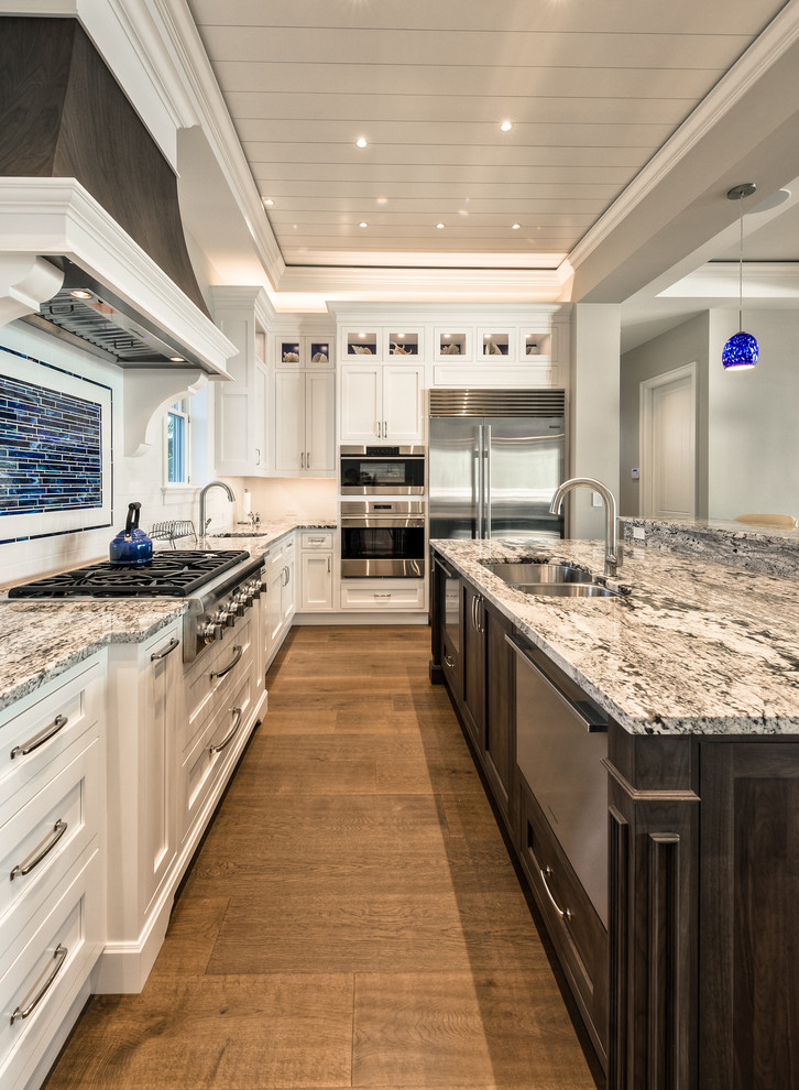 This is an example of a large traditional u-shaped open plan kitchen in Miami with a submerged sink, white cabinets, granite worktops, white splashback, ceramic splashback, stainless steel appliances, dark hardwood flooring and an island.