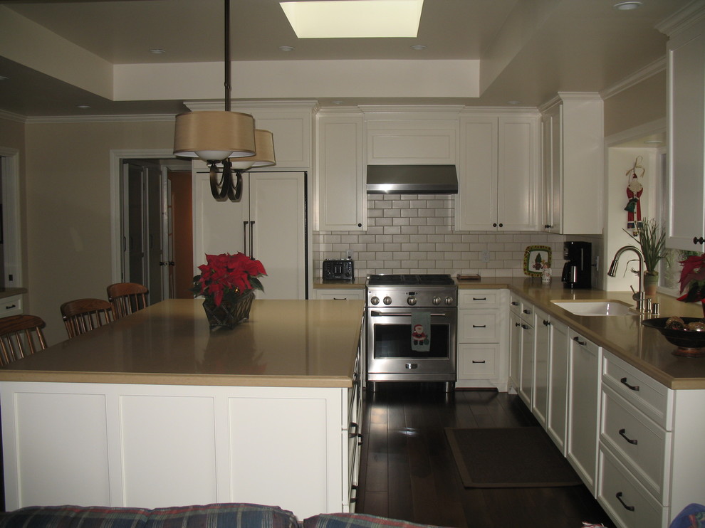 Inredning av ett amerikanskt kök, med en undermonterad diskho, luckor med infälld panel, vita skåp, bänkskiva i kvarts, vitt stänkskydd, stänkskydd i tunnelbanekakel och rostfria vitvaror