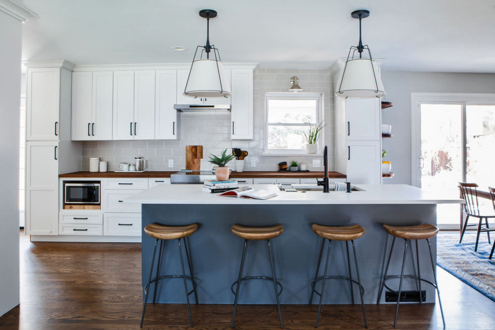 Inspiration for a mid-sized transitional galley medium tone wood floor and brown floor eat-in kitchen remodel in Denver with an undermount sink, shaker cabinets, white cabinets, quartz countertops, gray backsplash, ceramic backsplash, stainless steel appliances, an island and white countertops