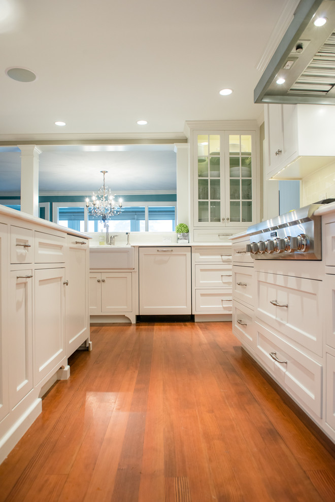 Inspiration for a large traditional l-shaped kitchen in Portland Maine with a built-in sink, recessed-panel cabinets, white cabinets, engineered stone countertops, white splashback, porcelain splashback, stainless steel appliances, medium hardwood flooring and an island.