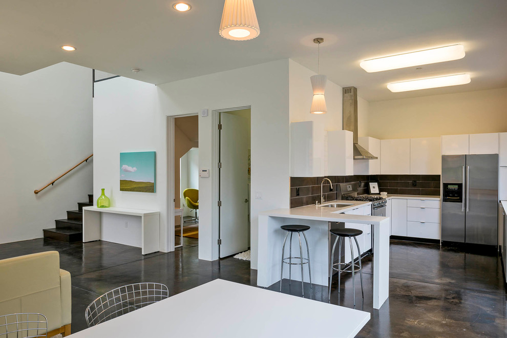 Идея дизайна: угловая кухня-гостиная в современном стиле с плоскими фасадами, белыми фасадами, черным фартуком и техникой из нержавеющей стали