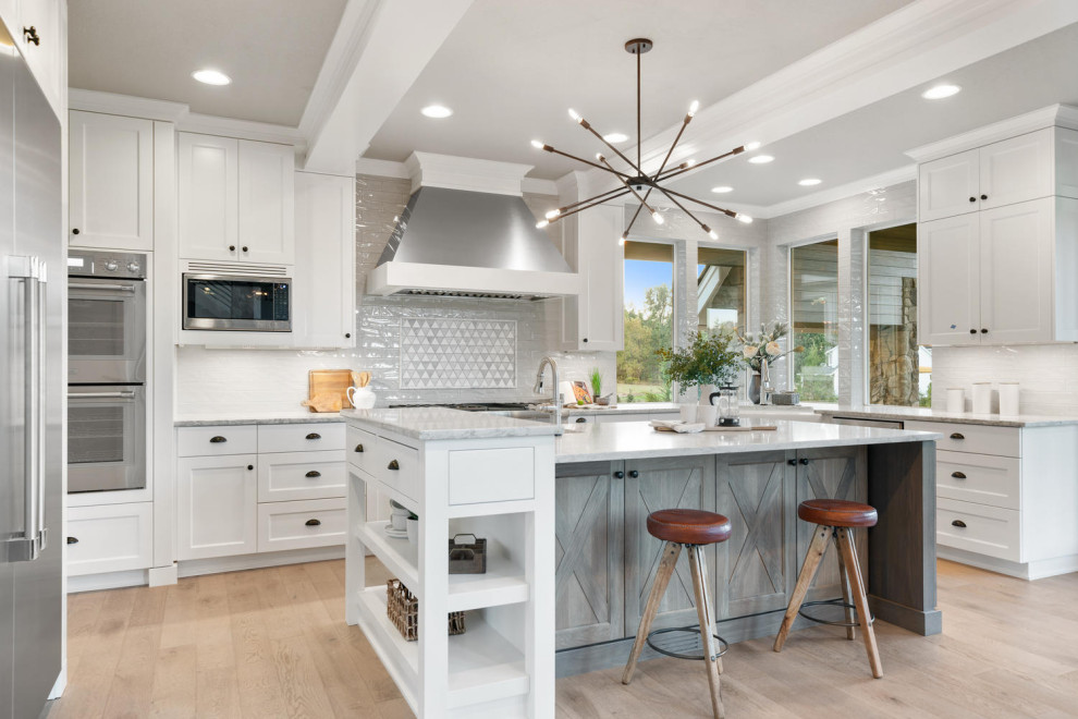Kitchen - large transitional u-shaped light wood floor and beige floor kitchen idea in Portland with a farmhouse sink, shaker cabinets, white cabinets, quartz countertops, gray backsplash, porcelain backsplash, stainless steel appliances, an island and gray countertops