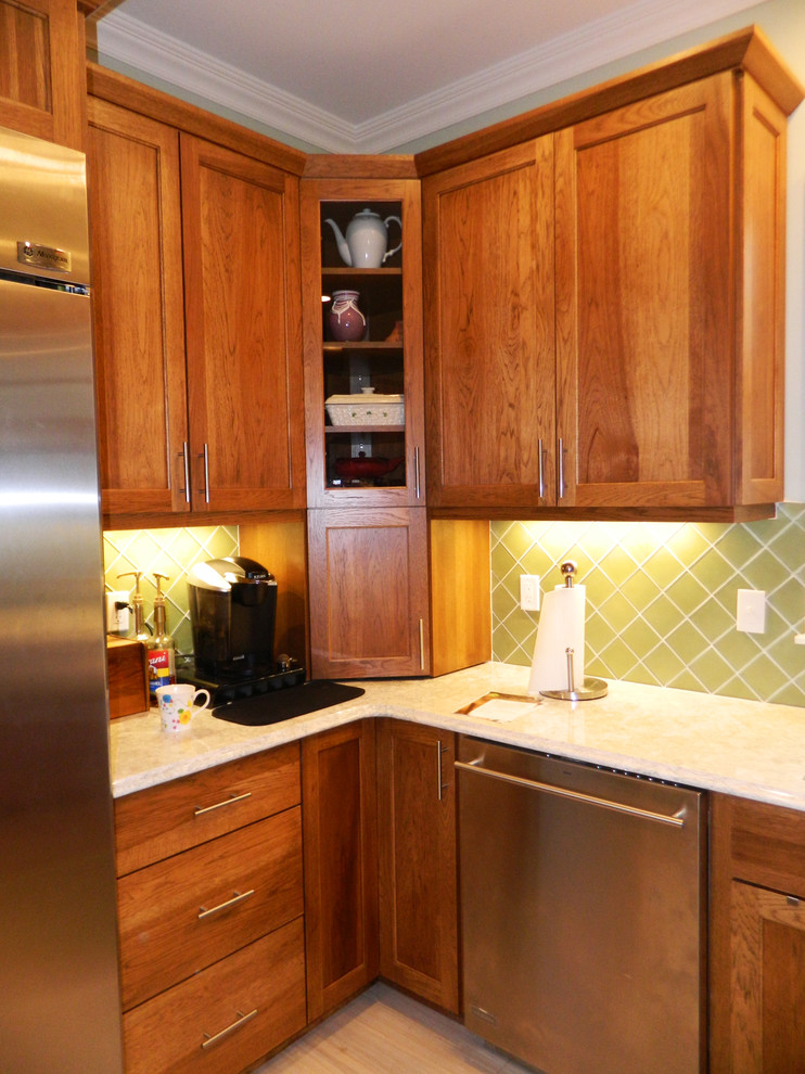 Inredning av ett modernt avskilt, litet l-kök, med en undermonterad diskho, skåp i shakerstil, skåp i mellenmörkt trä, granitbänkskiva, grönt stänkskydd, stänkskydd i glaskakel, rostfria vitvaror, klinkergolv i porslin och en halv köksö