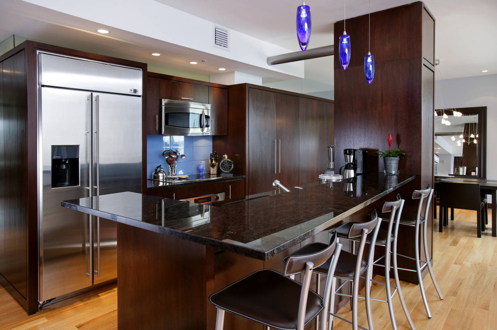 На фото: параллельная кухня в современном стиле с плоскими фасадами, темными деревянными фасадами, синим фартуком, техникой из нержавеющей стали и барной стойкой