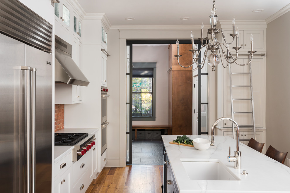 Inredning av ett retro mellanstort kök, med en undermonterad diskho, skåp i shakerstil, vita skåp, marmorbänkskiva, rött stänkskydd, rostfria vitvaror, mellanmörkt trägolv och en köksö