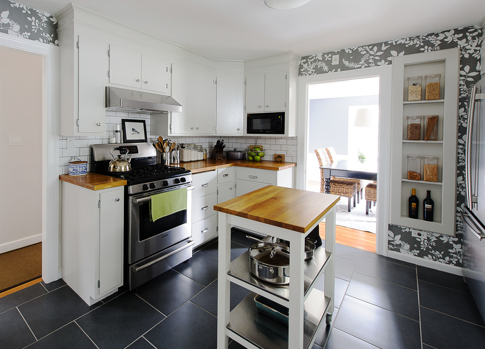 Classic enclosed kitchen in Boston with flat-panel cabinets, white cabinets, wood worktops, white splashback, metro tiled splashback, stainless steel appliances and black floors.