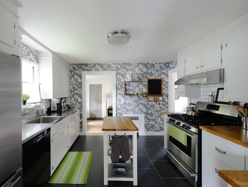 This is an example of a traditional enclosed kitchen in Boston with an integrated sink, flat-panel cabinets, white cabinets, stainless steel worktops, white splashback, metro tiled splashback and stainless steel appliances.