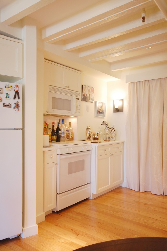 Cette image montre une petite cuisine linéaire traditionnelle avec un placard à porte shaker, des portes de placard blanches, une crédence blanche, une crédence en carrelage métro, un électroménager blanc, parquet clair et un sol beige.