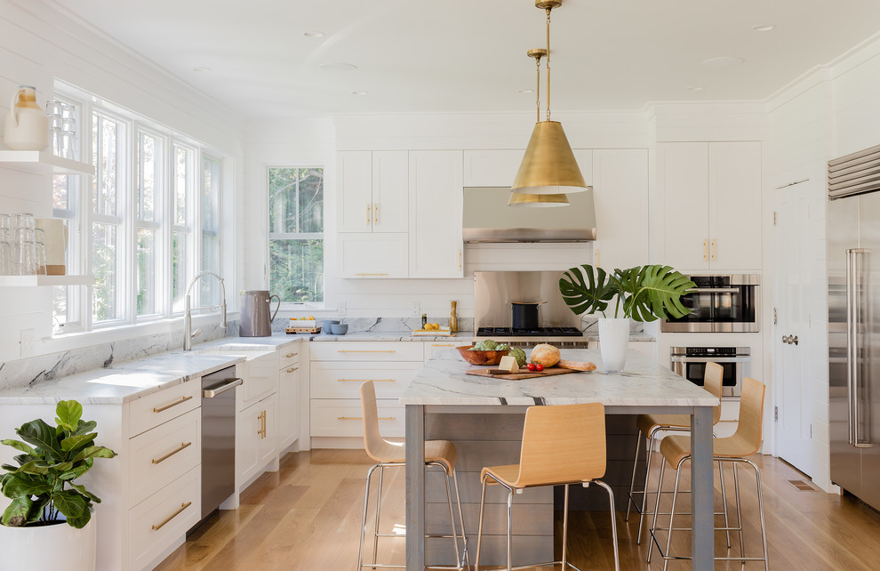Klassische Küche in U-Form mit Landhausspüle, Schrankfronten im Shaker-Stil, weißen Schränken, Küchengeräten aus Edelstahl, braunem Holzboden, Kücheninsel, braunem Boden und weißer Arbeitsplatte in Boston