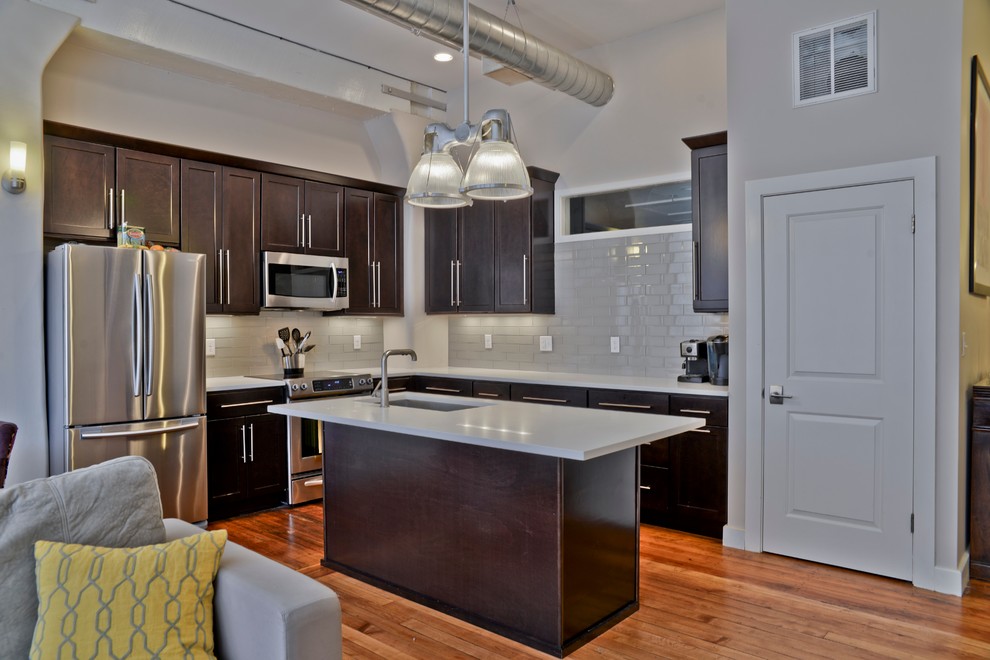Example of a mid-sized trendy l-shaped light wood floor eat-in kitchen design in Boston with an undermount sink, shaker cabinets, dark wood cabinets, quartzite countertops, gray backsplash, glass tile backsplash, stainless steel appliances and an island