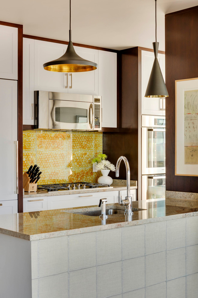 Bild på ett litet funkis parallellkök, med en undermonterad diskho, skåp i shakerstil, vita skåp, gult stänkskydd, rostfria vitvaror, en halv köksö och granitbänkskiva