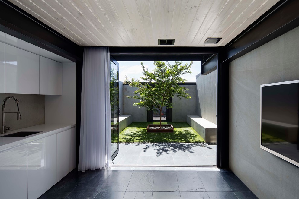 Cette image montre une cuisine linéaire minimaliste de taille moyenne avec un évier encastré, un placard à porte plane, des portes de placard blanches et un sol en ardoise.