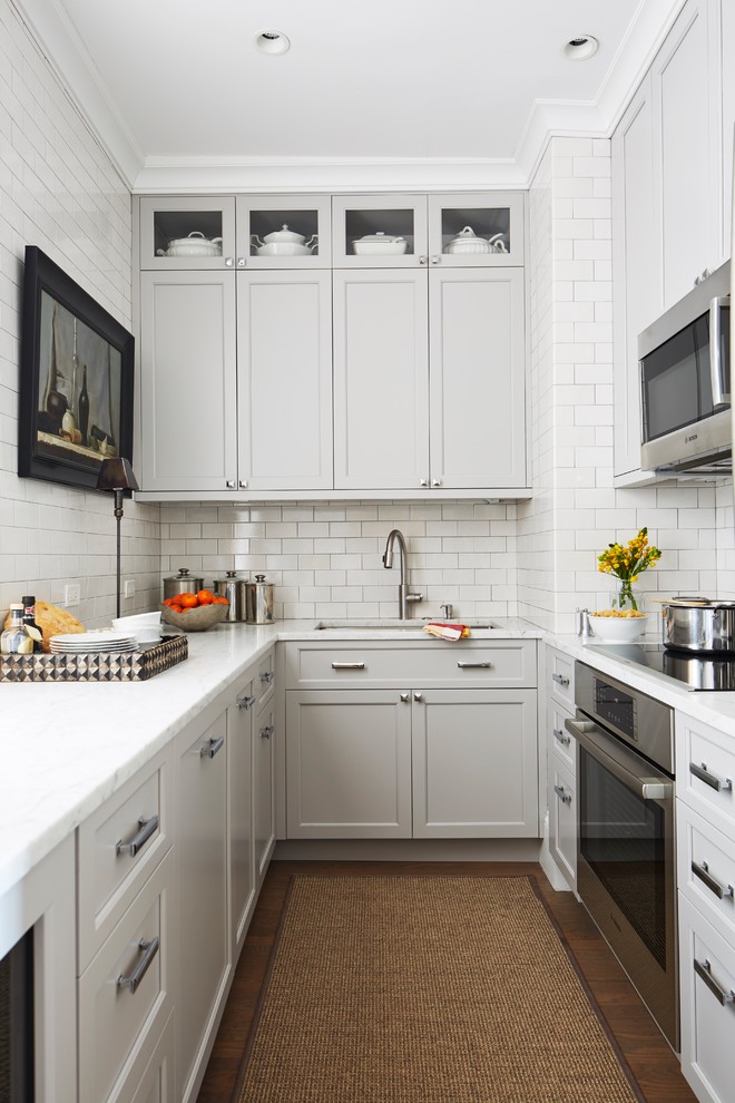 Inredning av ett klassiskt litet vit vitt kök, med en undermonterad diskho, grå skåp, marmorbänkskiva, vitt stänkskydd, skåp i shakerstil, stänkskydd i tunnelbanekakel, rostfria vitvaror och mörkt trägolv