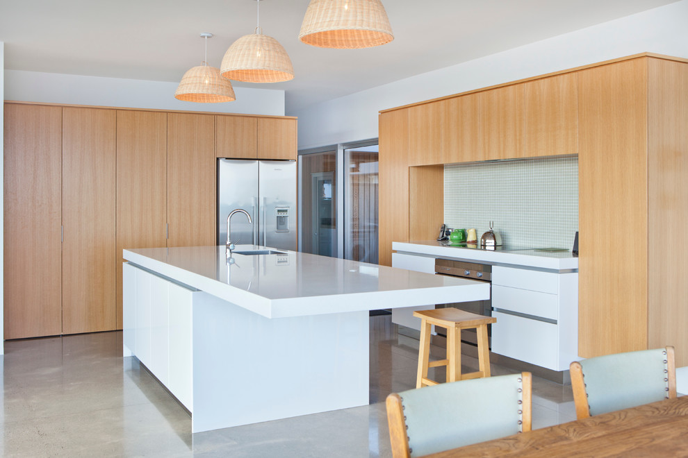 Идея дизайна: угловая кухня в современном стиле с обеденным столом, врезной мойкой, плоскими фасадами, светлыми деревянными фасадами, синим фартуком, техникой из нержавеющей стали, бетонным полом и островом