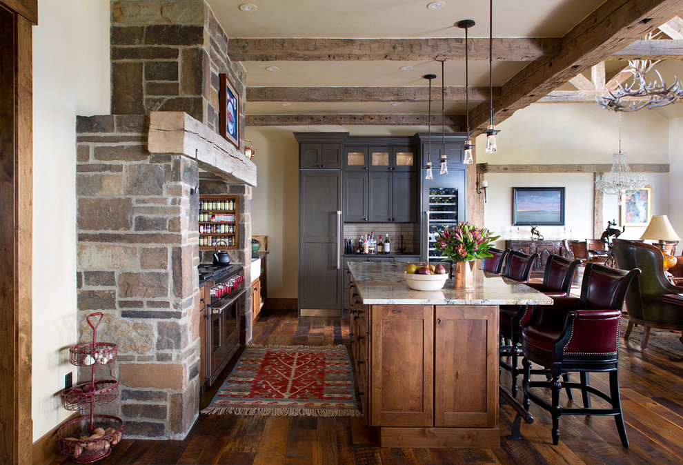 Inspiration for a large rustic l-shaped medium tone wood floor eat-in kitchen remodel in Denver with an undermount sink, shaker cabinets, brown cabinets, marble countertops, white backsplash, ceramic backsplash, paneled appliances and an island