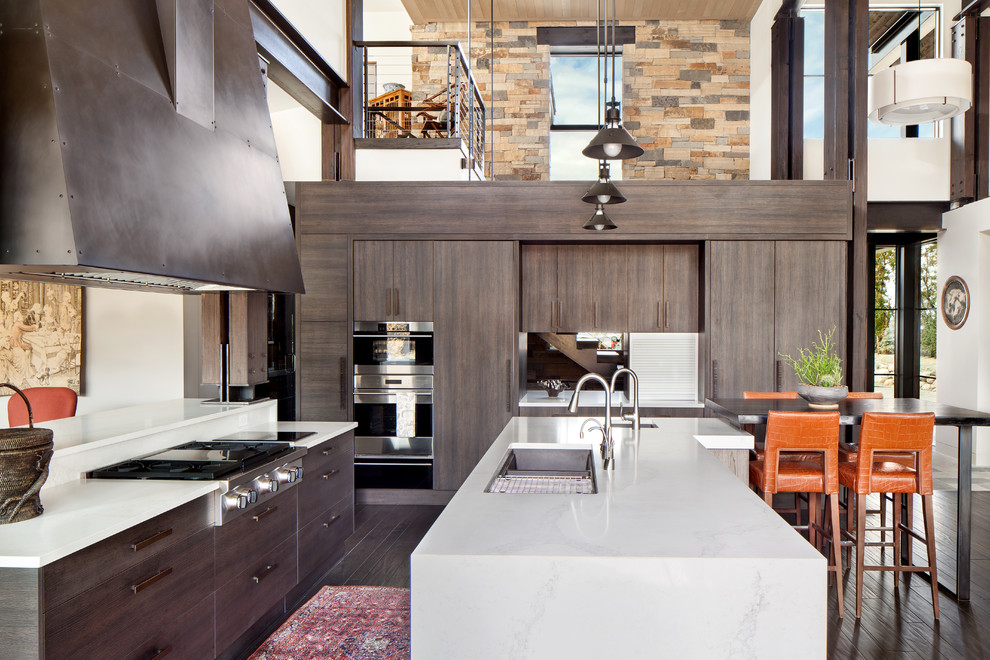 This is an example of a large traditional l-shaped open plan kitchen in Denver with a submerged sink, flat-panel cabinets, beige cabinets, engineered stone countertops, beige splashback, stone tiled splashback, stainless steel appliances, dark hardwood flooring, an island and brown floors.