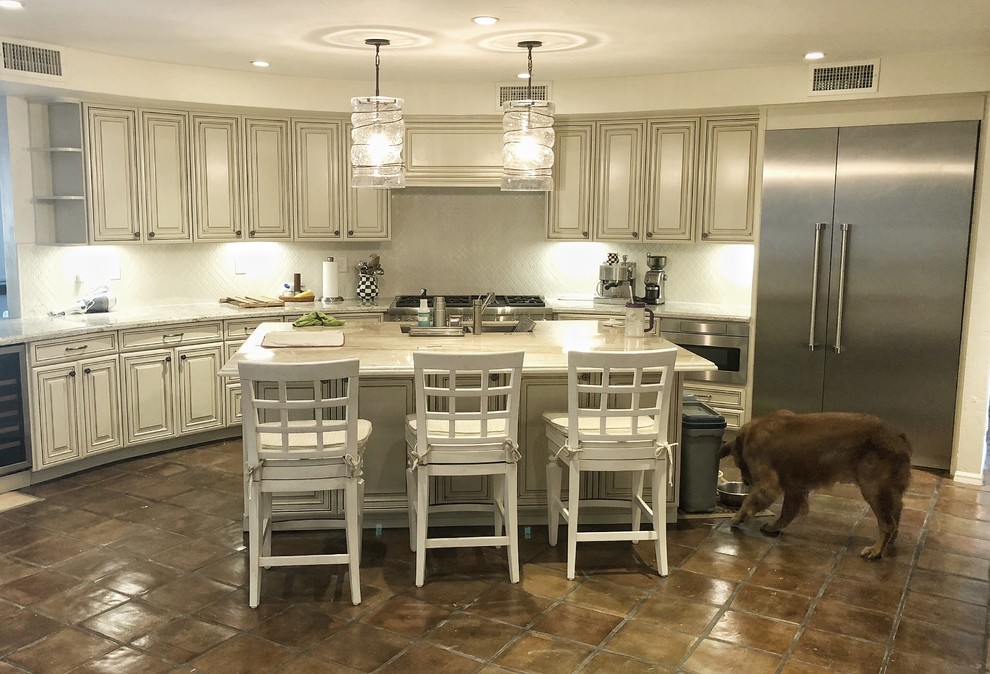 Klassisk inredning av ett mycket stort vit vitt kök, med en undermonterad diskho, luckor med upphöjd panel, vita skåp, bänkskiva i kvarts, vitt stänkskydd, stänkskydd i keramik, rostfria vitvaror, flera köksöar och brunt golv