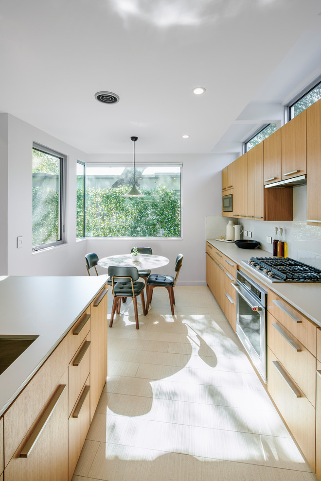 Inspiration for a mid-sized modern galley porcelain tile and gray floor eat-in kitchen remodel in Austin with an undermount sink, flat-panel cabinets, light wood cabinets, quartz countertops, white backsplash, glass sheet backsplash, stainless steel appliances, an island and gray countertops
