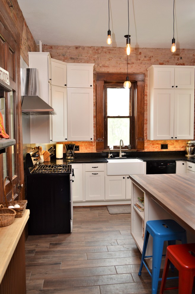 Exempel på ett avskilt, mellanstort lantligt svart svart u-kök, med en rustik diskho, luckor med infälld panel, vita skåp, bänkskiva i kvartsit, rött stänkskydd, stänkskydd i tegel, rostfria vitvaror, mellanmörkt trägolv, en köksö och brunt golv