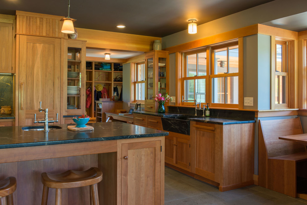Foto på ett stort amerikanskt linjärt kök och matrum, med en undermonterad diskho, luckor med infälld panel, skåp i mellenmörkt trä, bänkskiva i täljsten, svart stänkskydd, stänkskydd i sten, rostfria vitvaror, skiffergolv och en köksö