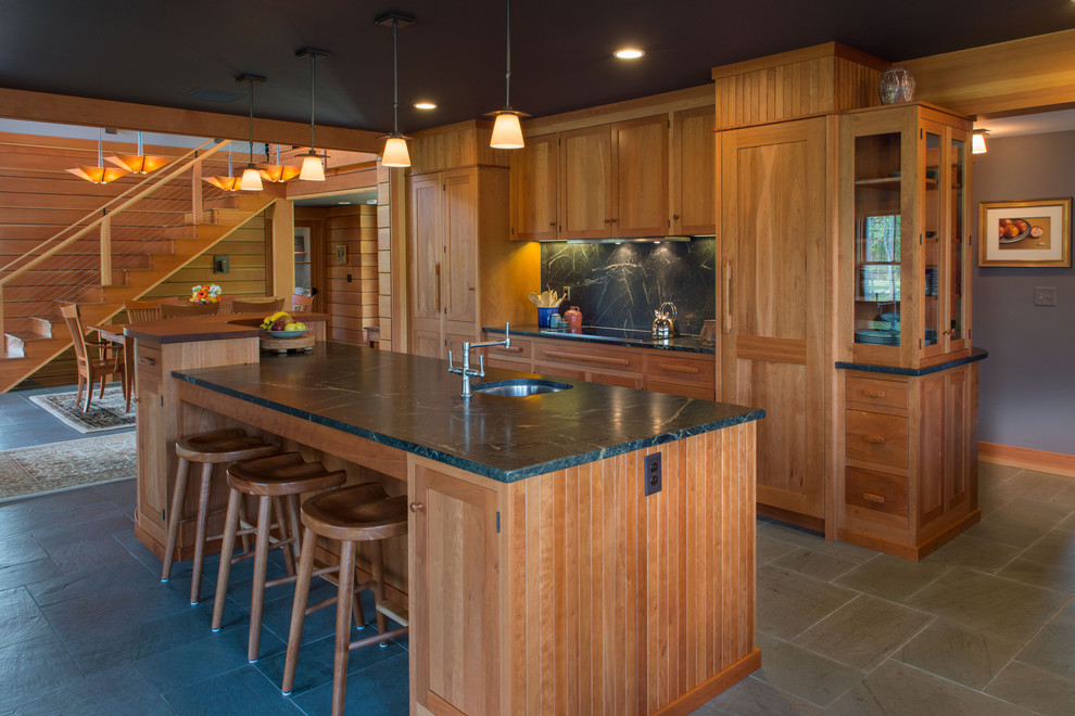 Exempel på ett stort amerikanskt linjärt kök och matrum, med en undermonterad diskho, luckor med infälld panel, skåp i mellenmörkt trä, bänkskiva i täljsten, svart stänkskydd, stänkskydd i sten, rostfria vitvaror, skiffergolv och en köksö