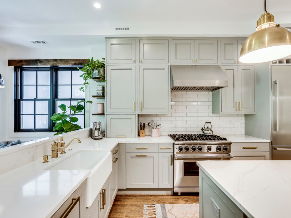 Bild på ett vintage vit vitt l-kök, med en rustik diskho, luckor med infälld panel, grå skåp, vitt stänkskydd, stänkskydd i tunnelbanekakel, rostfria vitvaror, mellanmörkt trägolv, en köksö och brunt golv