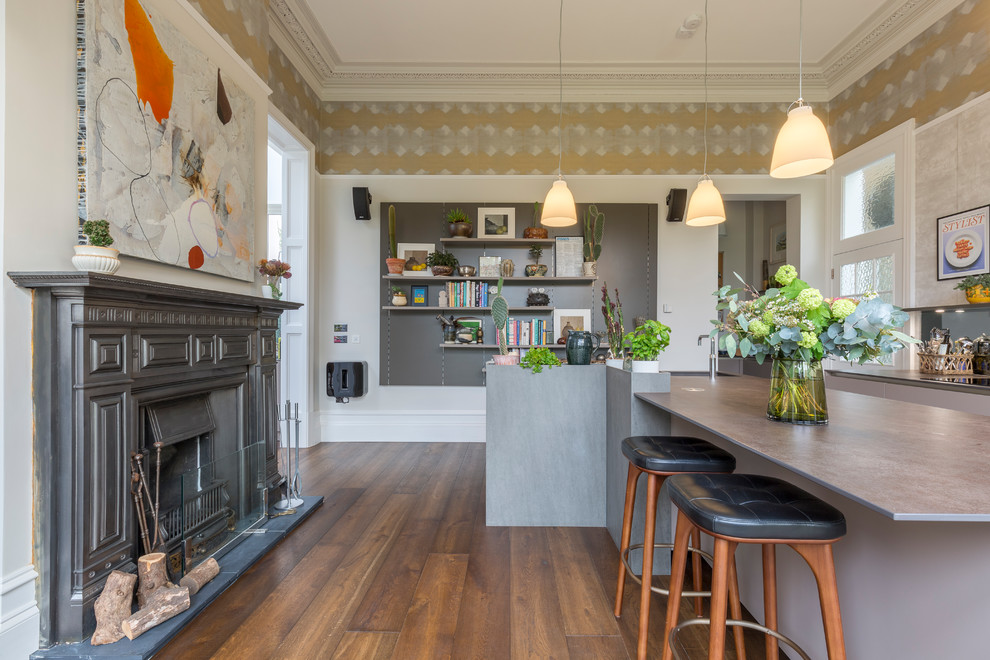Foto på ett mellanstort eklektiskt linjärt kök, med släta luckor, grå skåp, stänkskydd med metallisk yta, spegel som stänkskydd, rostfria vitvaror, mellanmörkt trägolv, en köksö och brunt golv