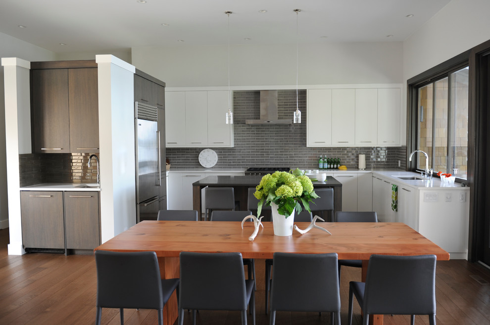 This is an example of a contemporary grey and white u-shaped open plan kitchen in Vancouver with a submerged sink, flat-panel cabinets, white cabinets, grey splashback, metro tiled splashback and stainless steel appliances.