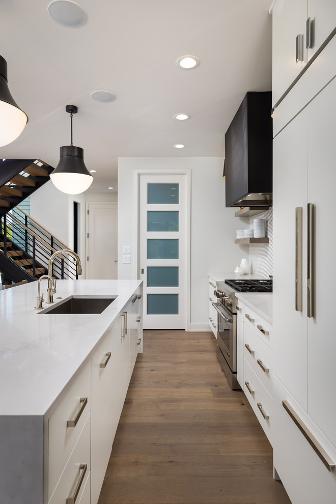 Photo of a contemporary single-wall kitchen/diner in Other with a single-bowl sink, flat-panel cabinets, white cabinets, engineered stone countertops, white splashback, ceramic splashback, white appliances, medium hardwood flooring, an island, grey floors and white worktops.