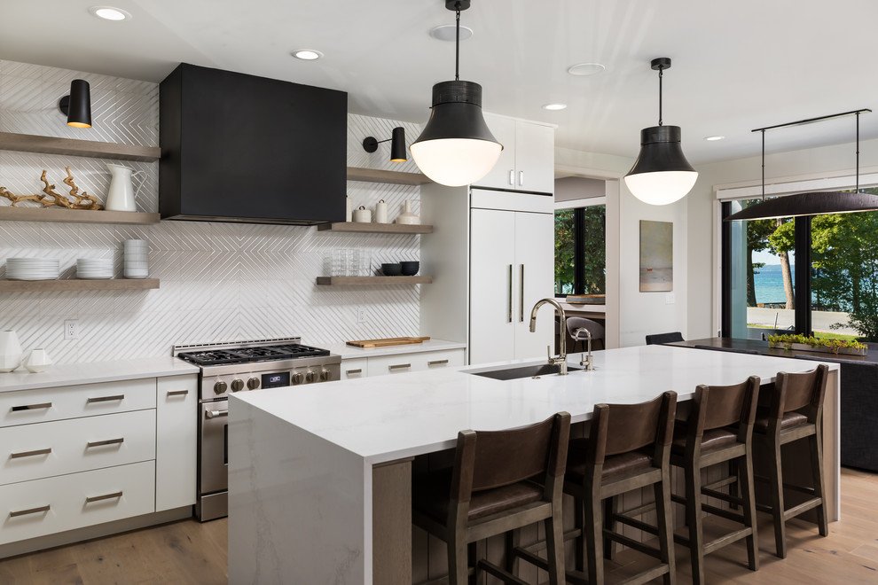 This is an example of a contemporary galley kitchen/diner in Other with a single-bowl sink, flat-panel cabinets, white cabinets, engineered stone countertops, white splashback, ceramic splashback, white appliances, medium hardwood flooring, an island, white worktops and brown floors.