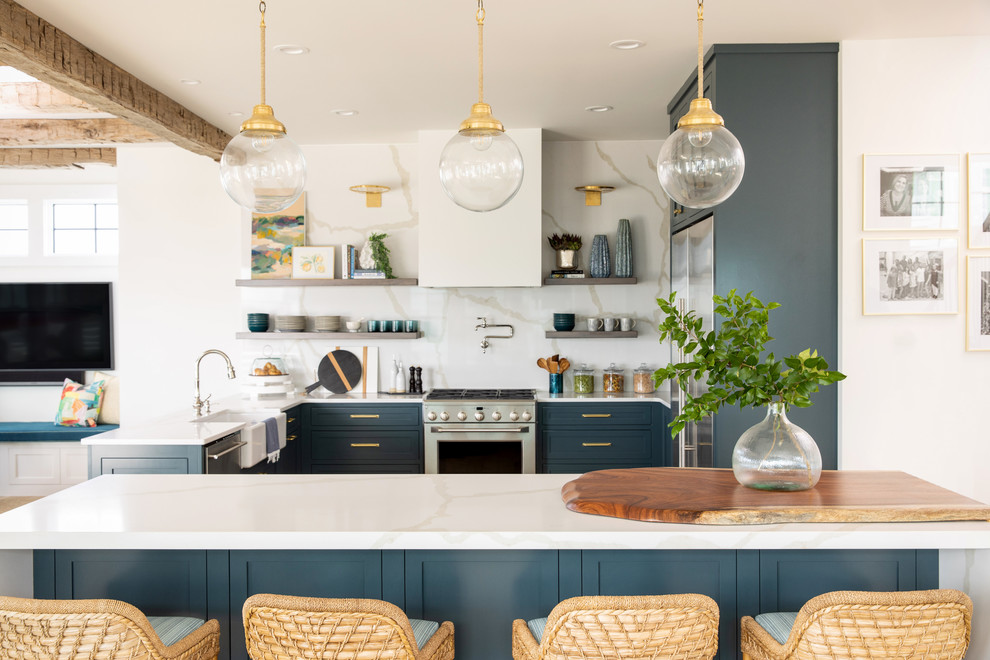 Inspiration for a coastal u-shaped open plan kitchen in Other with a belfast sink, shaker cabinets, blue cabinets, white splashback, stone slab splashback, stainless steel appliances, a breakfast bar and white worktops.