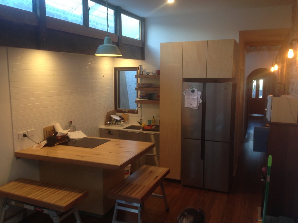 Foto på ett litet industriellt kök, med en enkel diskho, skåp i rostfritt stål, träbänkskiva, vitt stänkskydd, stänkskydd i tunnelbanekakel, rostfria vitvaror, bambugolv och en halv köksö