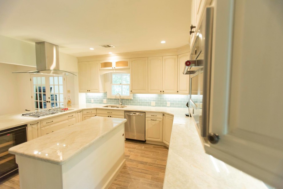 Foto på ett mellanstort vintage vit kök, med en undermonterad diskho, luckor med upphöjd panel, vita skåp, bänkskiva i kalksten, blått stänkskydd, stänkskydd i tunnelbanekakel, rostfria vitvaror, klinkergolv i porslin, en köksö och brunt golv