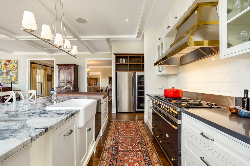 Klassisk inredning av ett kök, med en rustik diskho, luckor med infälld panel, vita skåp, svarta vitvaror, mörkt trägolv, en köksö och brunt golv