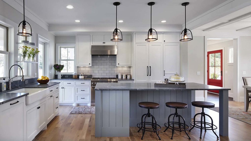 Example of a mid-sized cottage l-shaped light wood floor and beige floor eat-in kitchen design in Other with a farmhouse sink, shaker cabinets, white cabinets, white backsplash, subway tile backsplash, paneled appliances, an island and gray countertops