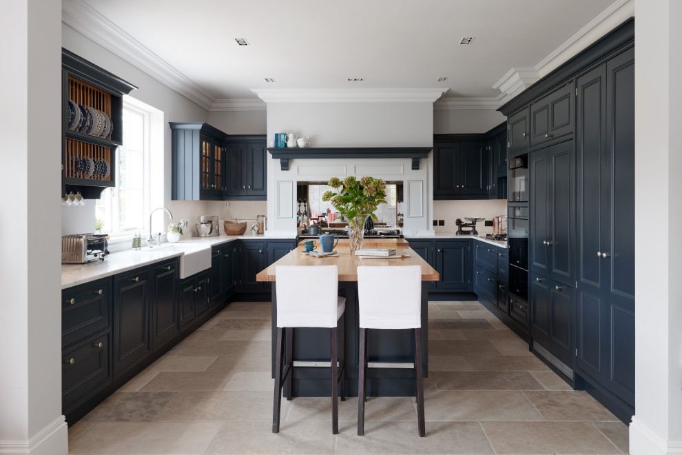 ウィルトシャーにある広いトラディショナルスタイルのおしゃれなキッチン (エプロンフロントシンク、落し込みパネル扉のキャビネット、青いキャビネット、白いキッチンパネル、パネルと同色の調理設備、ベージュの床、白いキッチンカウンター) の写真