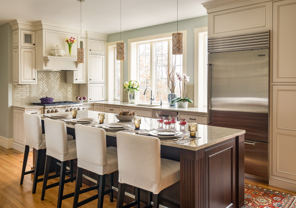 Kitchen - large traditional l-shaped light wood floor and brown floor kitchen idea in Boston with an undermount sink, recessed-panel cabinets, white cabinets, granite countertops, gray backsplash, glass tile backsplash, stainless steel appliances, an island and beige countertops