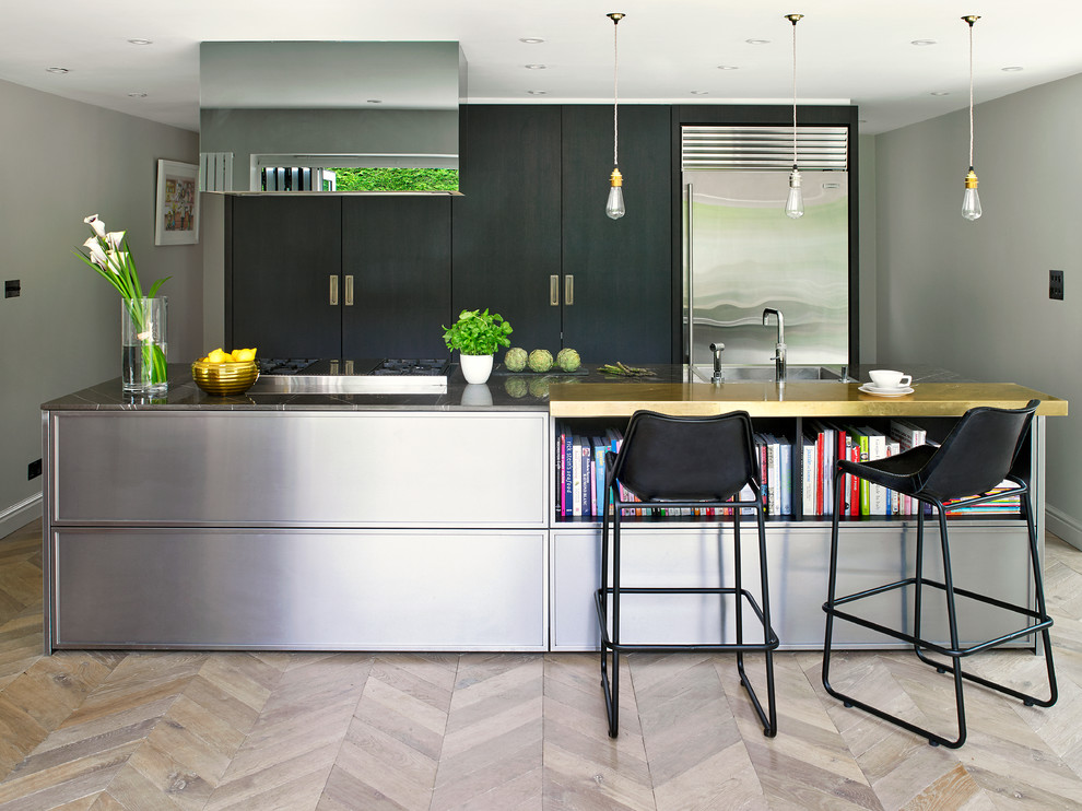 Design ideas for a contemporary galley kitchen/diner in London with a single-bowl sink, flat-panel cabinets, black cabinets, stainless steel worktops, light hardwood flooring, an island and stainless steel appliances.