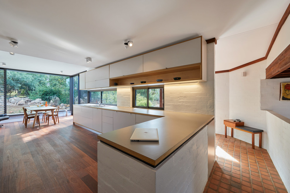 Moderne Wohnküche in L-Form mit weißen Schränken, Laminat-Arbeitsplatte, Rückwand-Fenster, Doppelwaschbecken, Küchengeräten aus Edelstahl, dunklem Holzboden, rotem Boden und Küchenrückwand in Weiß in Perth