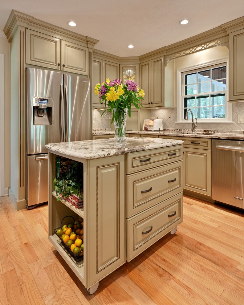 Foto på ett mellanstort vintage beige kök, med luckor med upphöjd panel, rostfria vitvaror, en undermonterad diskho, gröna skåp, granitbänkskiva, beige stänkskydd, stänkskydd i stenkakel, ljust trägolv, en köksö och brunt golv