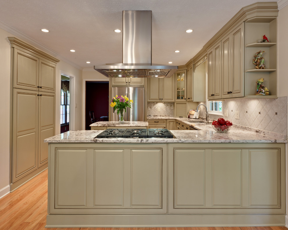 Example of a mid-sized classic u-shaped light wood floor and brown floor eat-in kitchen design in Atlanta with stainless steel appliances, raised-panel cabinets, an undermount sink, green cabinets, granite countertops, beige backsplash, stone tile backsplash, an island and beige countertops